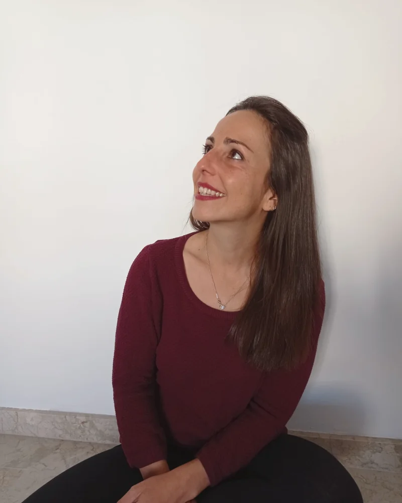 Estefanía sonriendo, sentada en su espacio, con un jersey granate